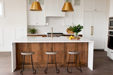 Example of a mid-sized cottage l-shaped brown floor and dark wood floor kitchen design in Boise with a farmhouse sink, shaker cabinets, quartz countertops, white backsplash, mosaic tile backsplash, stainless steel appliances, an island, white countertops and white cabinets