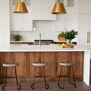 Mid-sized farmhouse kitchen inspiration - Example of a mid-sized cottage l-shaped medium tone wood floor and brown floor kitchen design in Boise with a farmhouse sink, shaker cabinets, medium tone wood cabinets, quartz countertops, white backsplash, mosaic tile backsplash, stainless steel appliances, an island and white countertops