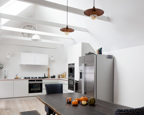 Large contemporary l-shaped kitchen/diner in London with flat-panel cabinets, white cabinets, stainless steel appliances, light hardwood flooring, no island, beige floors and a submerged sink.