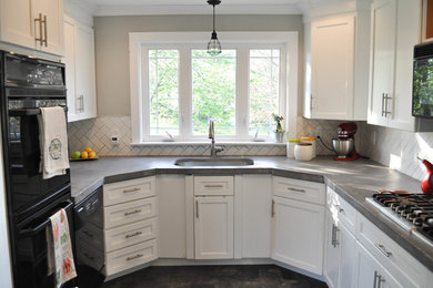 Photo of a mid-sized country u-shaped kitchen in Philadelphia with an undermount sink, shaker cabinets, white cabinets, concrete benchtops, white splashback, subway tile splashback, black appliances, no island and grey floor.