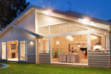 This is an example of a large beach style two-storey beige house exterior in Sydney with wood siding, a flat roof and a metal roof.