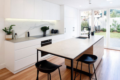Inspiration for a small modern galley open plan kitchen in Sydney with an undermount sink, flat-panel cabinets, white cabinets, solid surface benchtops, white splashback, porcelain splashback, black appliances, medium hardwood floors, with island, grey floor and beige benchtop.
