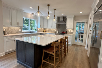Large transitional l-shaped laminate floor and gray floor kitchen photo in New York with an undermount sink, shaker cabinets, white cabinets, quartz countertops, gray backsplash, porcelain backsplash, stainless steel appliances, an island and white countertops
