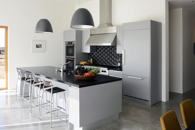 Photo of a modern kitchen in Albuquerque with an undermount sink, flat-panel cabinets, grey cabinets, granite benchtops, black splashback, ceramic splashback, stainless steel appliances, concrete floors, with island and grey floor.