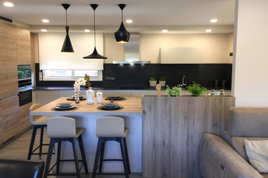 Modelo de cocina mediterránea con fregadero bajoencimera, puertas de armario de madera clara, salpicadero negro, suelo de baldosas de porcelana y una isla
