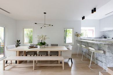 This is an example of a contemporary kitchen/dining combo in Sydney with white walls, light hardwood floors and beige floor.