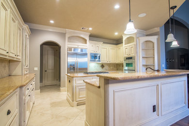 Expansive traditional kitchen pantry in Houston with a double-bowl sink, raised-panel cabinets, distressed cabinets, granite benchtops, beige splashback, stone tile splashback, stainless steel appliances, travertine floors and with island.