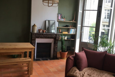 Réalisation d'un salon bohème de taille moyenne et ouvert avec un mur vert, tomettes au sol, une cheminée standard, un manteau de cheminée en pierre de parement et un sol orange.
