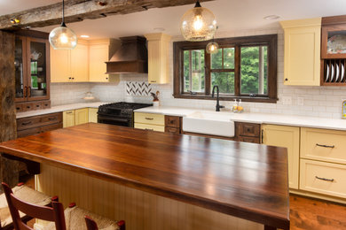 ポートランド(メイン)にある高級な広いカントリー風のおしゃれなキッチン (エプロンフロントシンク、シェーカースタイル扉のキャビネット、黄色いキャビネット、クオーツストーンカウンター、白いキッチンパネル、サブウェイタイルのキッチンパネル、シルバーの調理設備、濃色無垢フローリング、茶色い床、白いキッチンカウンター) の写真