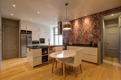 Cette image montre une grande cuisine ouverte design en L avec un évier encastré, un placard à porte affleurante, des portes de placard blanches, un plan de travail en quartz, une crédence grise, un électroménager en acier inoxydable, parquet clair et îlot.