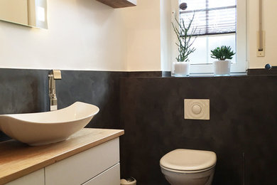 Kleine Moderne Gästetoilette mit flächenbündigen Schrankfronten, weißen Schränken, Wandtoilette, schwarzen Fliesen, weißer Wandfarbe, Aufsatzwaschbecken, Waschtisch aus Holz, braunem Boden und brauner Waschtischplatte in Nürnberg