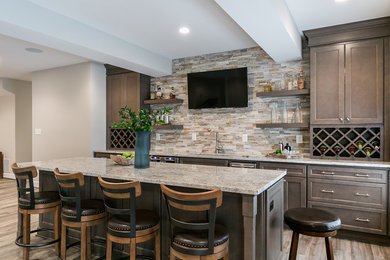 Design ideas for a large transitional single-wall seated home bar in DC Metro with brown cabinets, granite benchtops, beige splashback, stone tile splashback, laminate floors, brown floor, recessed-panel cabinets, an undermount sink and grey benchtop.