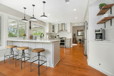 Inspiration for a large country u-shaped medium tone wood floor and brown floor kitchen remodel in Orange County with a farmhouse sink, shaker cabinets, white cabinets, quartzite countertops, white backsplash, subway tile backsplash, stainless steel appliances, no island and white countertops