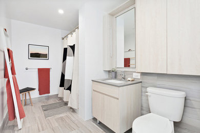 Example of a mid-sized trendy 3/4 porcelain tile and beige floor bathroom design in New York with flat-panel cabinets, light wood cabinets, a two-piece toilet, white walls, an undermount sink and gray countertops