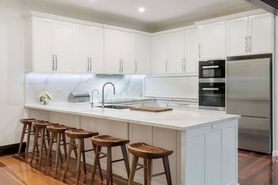 Inspiration for a large traditional u-shaped kitchen pantry in Sydney with a single-bowl sink, shaker cabinets, white cabinets, quartz benchtops, white splashback, stone slab splashback, stainless steel appliances, dark hardwood floors, no island, brown floor and white benchtop.