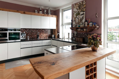 Große Klassische Küche in U-Form mit Einbauwaschbecken, flächenbündigen Schrankfronten, weißen Schränken, Arbeitsplatte aus Holz, Küchenrückwand in Braun, Rückwand aus Mosaikfliesen, Küchengeräten aus Edelstahl, braunem Holzboden und Halbinsel in München