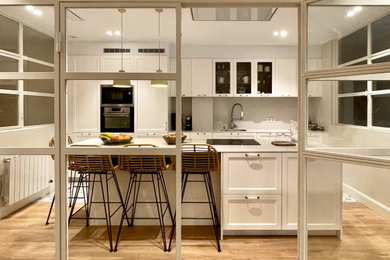 Imagen de cocina tradicional abierta con armarios con paneles con relieve, puertas de armario blancas, una isla y encimeras blancas