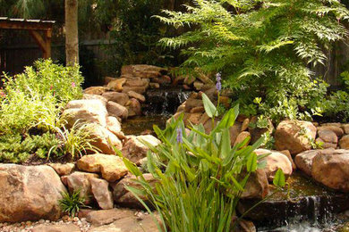 Photo of a mid-sized traditional backyard stone pond in Oklahoma City.