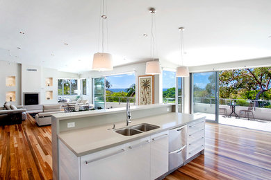 Mid-sized modern open plan kitchen in Brisbane with a double-bowl sink, flat-panel cabinets, white cabinets, solid surface benchtops, stainless steel appliances, medium hardwood floors and with island.
