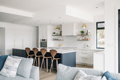 Photo of a large contemporary l-shaped open plan kitchen in Edmonton with a submerged sink, shaker cabinets, white cabinets, glass worktops, white splashback, engineered quartz splashback, integrated appliances, medium hardwood flooring, an island and white worktops.