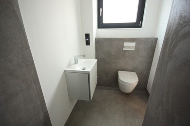 Contemporary powder room in Other with a two-piece toilet, gray tile, ceramic tile, grey walls, a drop-in sink and grey floor.