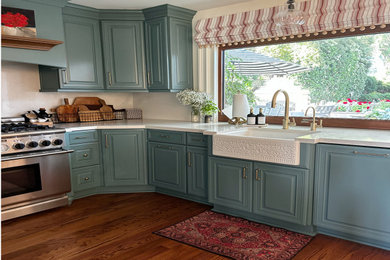 Mid-sized transitional u-shaped medium tone wood floor and brown floor eat-in kitchen photo in San Diego with a farmhouse sink, raised-panel cabinets, green cabinets, solid surface countertops, white backsplash, quartz backsplash, colored appliances, an island and white countertops