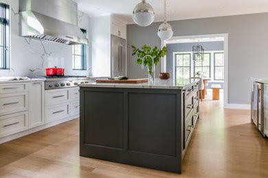 Large country kitchen pantry in Boston with an undermount sink, shaker cabinets, white cabinets, quartz benchtops, white splashback, stone slab splashback, stainless steel appliances, light hardwood floors, multiple islands and white benchtop.