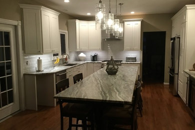 Inspiration for a mid-sized transitional u-shaped medium tone wood floor and brown floor open concept kitchen remodel in DC Metro with an undermount sink, white cabinets, granite countertops, white backsplash, subway tile backsplash, stainless steel appliances, an island, gray countertops and shaker cabinets