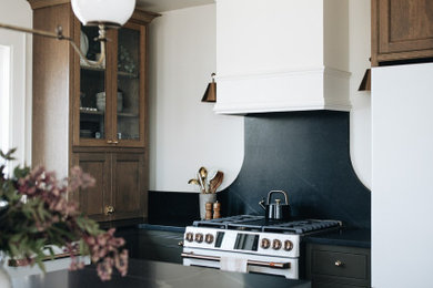 Eat-in kitchen - mid-sized french country l-shaped eat-in kitchen idea in Minneapolis with a farmhouse sink, beaded inset cabinets, dark wood cabinets, granite countertops, black backsplash, granite backsplash, white appliances, an island and black countertops