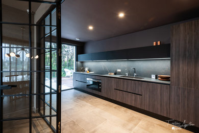 Exemple d'une grande cuisine ouverte linéaire tendance en bois foncé avec un évier encastré, un placard à porte affleurante, un plan de travail en surface solide, une crédence noire, une crédence en marbre, un électroménager noir, sol en béton ciré, aucun îlot, un sol gris et un plan de travail gris.
