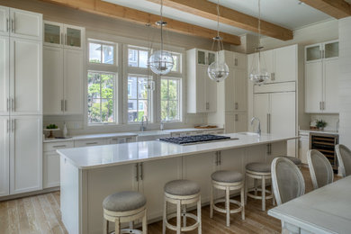 Design ideas for a mid-sized beach style l-shaped kitchen in Other with a farmhouse sink, shaker cabinets, white cabinets, panelled appliances, medium hardwood floors, with island, brown floor, white benchtop and exposed beam.