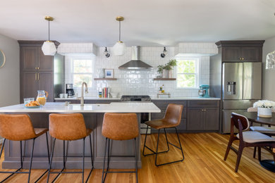 Transitional medium tone wood floor kitchen photo in Boston with a farmhouse sink, flat-panel cabinets, gray cabinets, quartz countertops, white backsplash, ceramic backsplash, stainless steel appliances, an island and white countertops