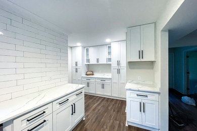 Example of a large minimalist galley vinyl floor kitchen design in Other with a single-bowl sink, shaker cabinets, white cabinets, quartz countertops, white backsplash, ceramic backsplash, stainless steel appliances, an island and white countertops