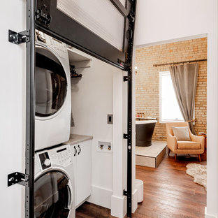 Inspiration for a small urban single-wall laundry cupboard in Other with flat-panel cabinets, white cabinets, laminate countertops, laminate floors, a stacked washer and dryer, grey worktops, white walls and brown floors.