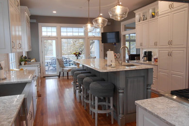 Example of a mid-sized trendy u-shaped medium tone wood floor and brown floor open concept kitchen design in Other with a farmhouse sink, raised-panel cabinets, white cabinets, granite countertops, gray backsplash, matchstick tile backsplash, stainless steel appliances, an island and gray countertops