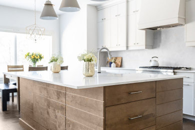 Example of a mid-sized trendy l-shaped dark wood floor and brown floor eat-in kitchen design in Calgary with a farmhouse sink, gray cabinets, quartz countertops, gray backsplash, stainless steel appliances, an island and white countertops