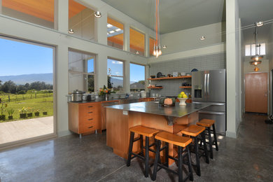 Design ideas for a mid-sized industrial l-shaped open plan kitchen in Hawaii with a farmhouse sink, stainless steel appliances, concrete floors, grey floor, grey splashback, ceramic splashback, grey benchtop, flat-panel cabinets, medium wood cabinets, stainless steel benchtops and with island.