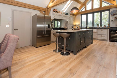 This is an example of a large country u-shaped eat-in kitchen in Surrey with a farmhouse sink, shaker cabinets, grey cabinets, granite benchtops, black splashback, stainless steel appliances, light hardwood floors and with island.