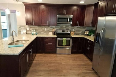 Open concept kitchen - mid-sized contemporary u-shaped laminate floor and brown floor open concept kitchen idea in Tampa with an undermount sink, shaker cabinets, dark wood cabinets, granite countertops, multicolored backsplash, glass tile backsplash, stainless steel appliances and a peninsula