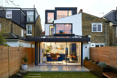 Large and white modern rear and render house exterior in London with three floors, a black roof and a mansard roof.