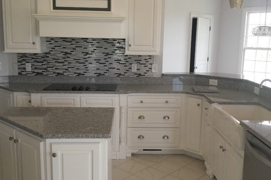 Example of a mid-sized transitional u-shaped white floor enclosed kitchen design in Nashville with a farmhouse sink, raised-panel cabinets, white cabinets, granite countertops, multicolored backsplash, glass tile backsplash, stainless steel appliances and an island