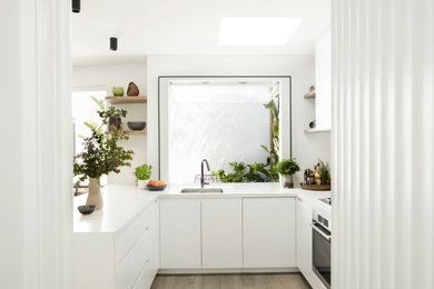This is an example of a mid-sized contemporary u-shaped open plan kitchen in Melbourne with an undermount sink, flat-panel cabinets, white cabinets, quartz benchtops, grey splashback, stone slab splashback, stainless steel appliances, medium hardwood floors, a peninsula, brown floor and white benchtop.