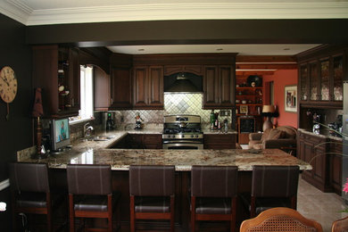Elegant kitchen photo in Toronto with raised-panel cabinets, dark wood cabinets, stainless steel appliances and an island