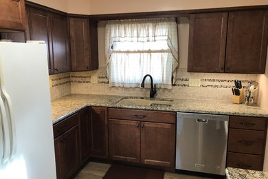Mid-sized elegant l-shaped vinyl floor and multicolored floor enclosed kitchen photo in Other with an undermount sink, recessed-panel cabinets, brown cabinets, granite countertops, multicolored backsplash and mosaic tile backsplash