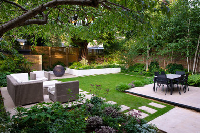Contemporary back partial sun garden in London with natural stone paving and a wood fence.