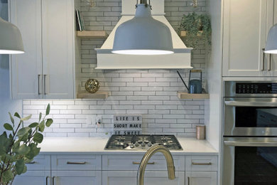 Example of a mid-sized trendy l-shaped vinyl floor eat-in kitchen design in Calgary with a farmhouse sink, shaker cabinets, white cabinets, quartz countertops, white backsplash, subway tile backsplash, stainless steel appliances, an island and white countertops