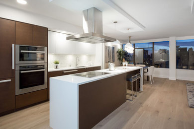 Mid-sized transitional galley medium tone wood floor and brown floor open concept kitchen photo in Vancouver with a drop-in sink, flat-panel cabinets, white cabinets, solid surface countertops, gray backsplash and an island