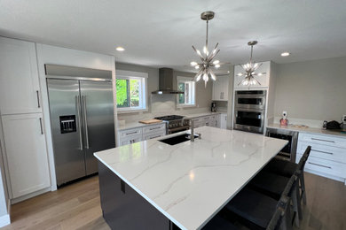 Inspiration for a large modern galley laminate floor and brown floor eat-in kitchen remodel in Denver with an undermount sink, shaker cabinets, white cabinets, marble countertops, white backsplash, marble backsplash, stainless steel appliances, an island and white countertops
