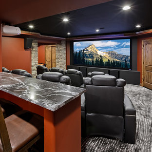 This is an example of a large traditional enclosed home cinema in Denver with orange walls, carpet, a projector screen and grey floors.