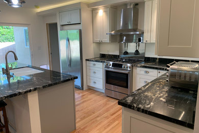 Open concept kitchen - mid-sized contemporary l-shaped medium tone wood floor, brown floor and tray ceiling open concept kitchen idea in Los Angeles with an undermount sink, shaker cabinets, white cabinets, granite countertops, stainless steel appliances, an island and black countertops